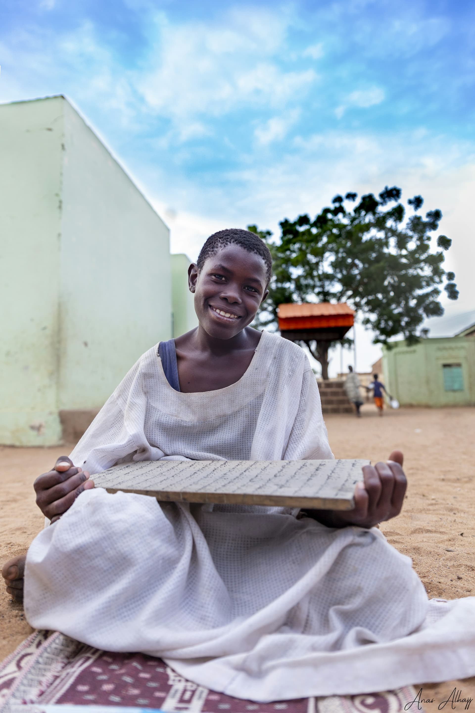 Un enfant souriant tient une tablette d'écriture en bois